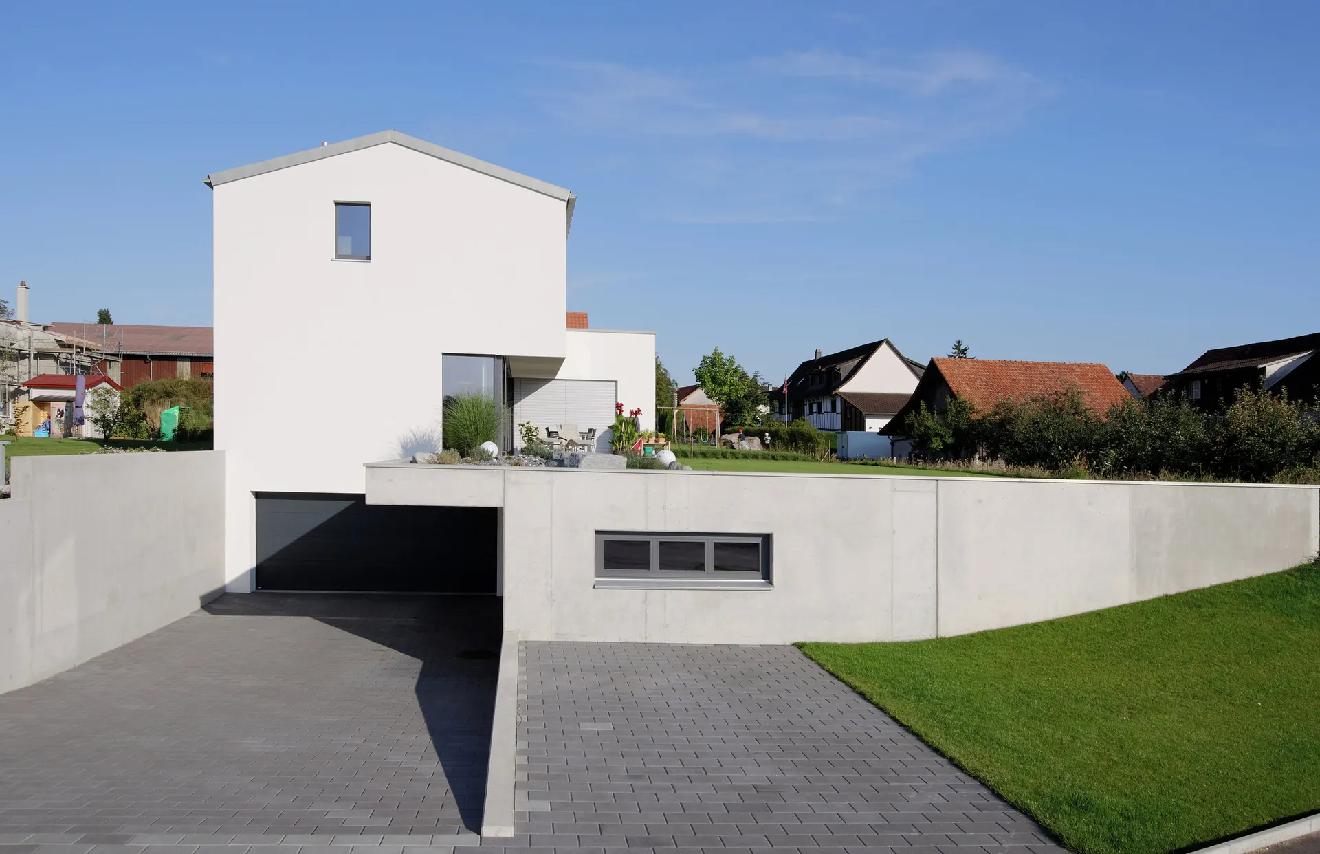 Einfamilienhaus in Neuwilen mit hellem Hauptbaukörper über einem Betonsockel.