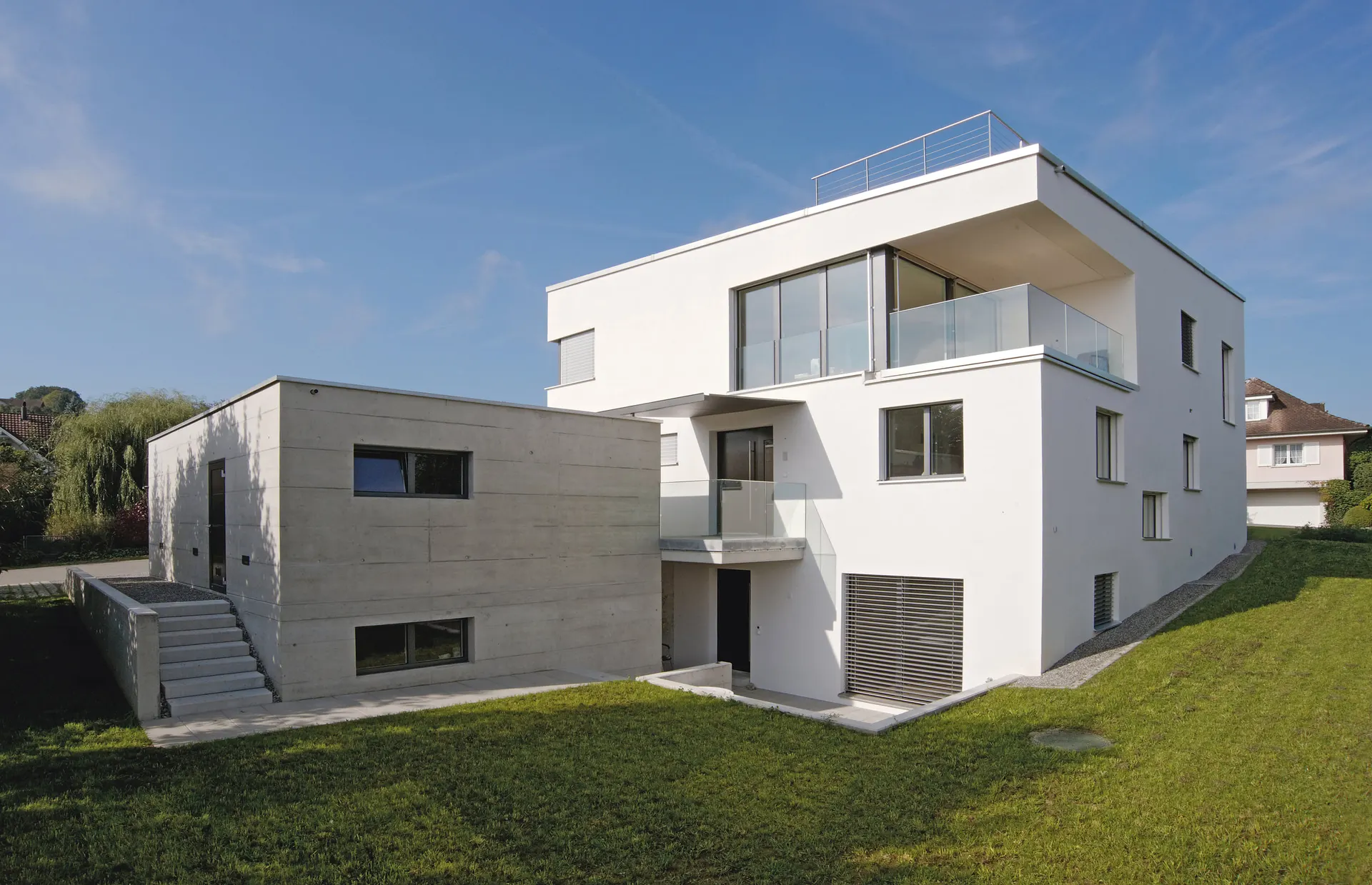 Rückwärtige Ansicht des Hauses mit Eckverglasung und niedrigem Betonbaukörper.