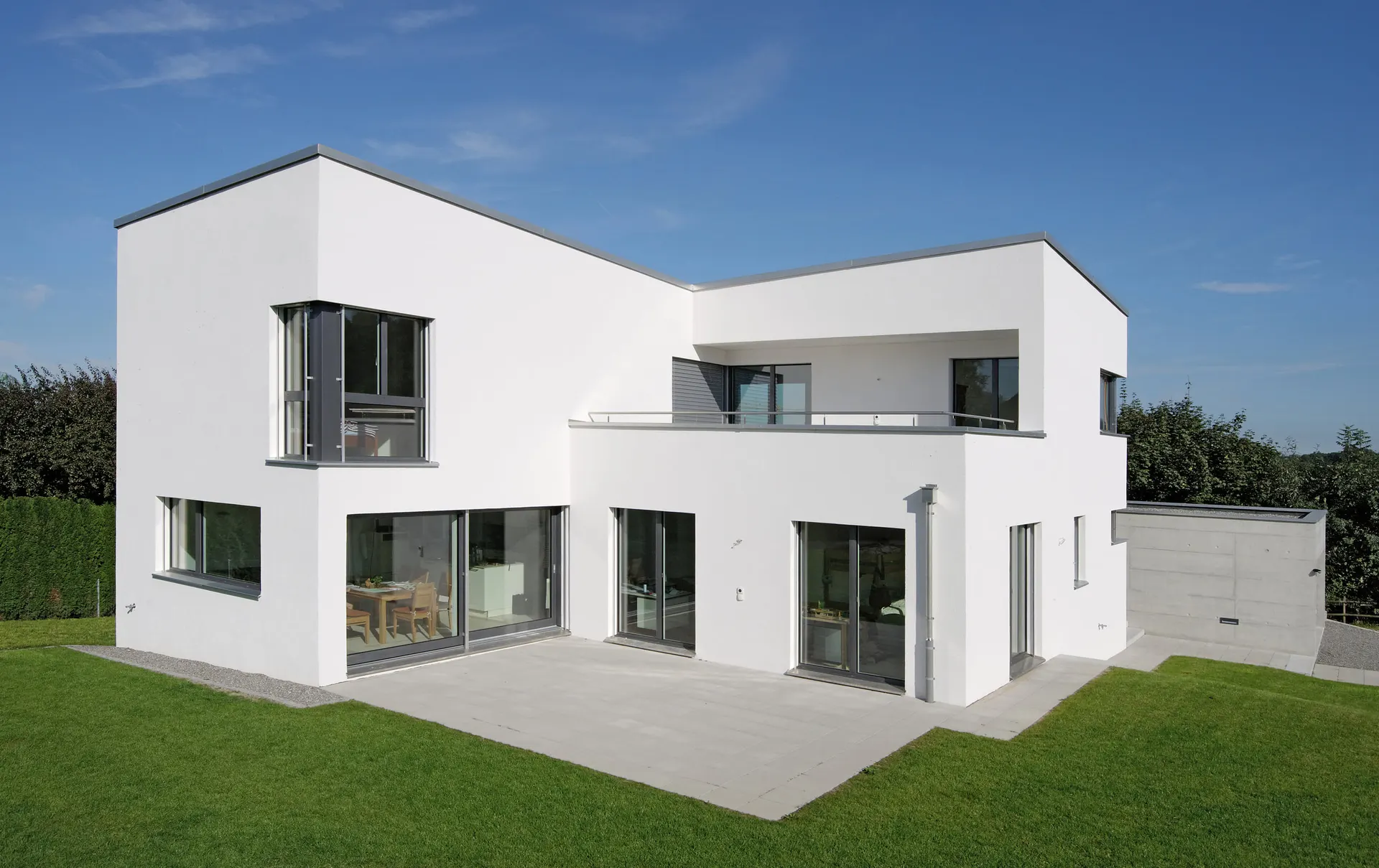 Gartenfassade mit grosser Verglasung, Terrasse und zurückliegendem Obergeschoss.