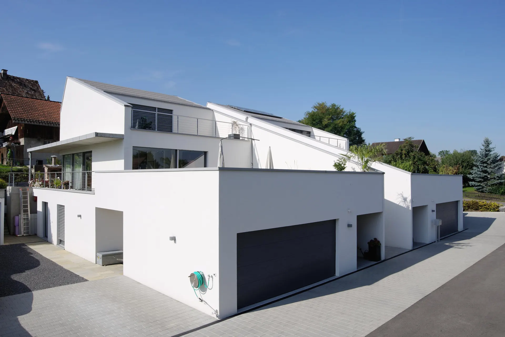 Strassenansicht mit geschlossenem Sockel und darüberliegenden geneigten Dachlinien.