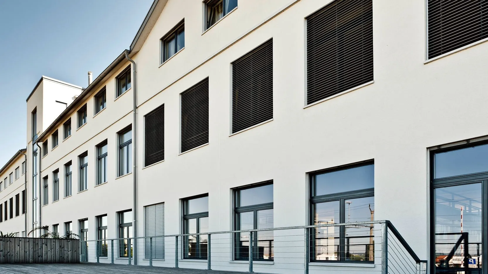 Lange Fabrikfassade mit neuen Balkonen vor der regelmässigen Fensterstruktur.