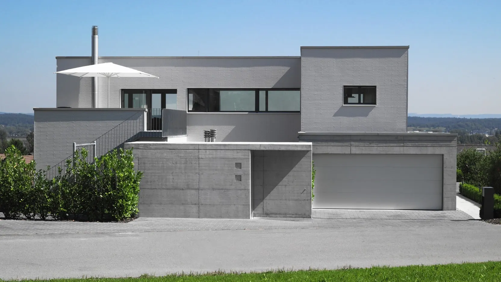 Haus der klaren Ebenen in Tägerwilen mit gestaffelten weissen Fassaden, erhöhtem Aussenraum und vorgelagertem Sichtbetonsockel.