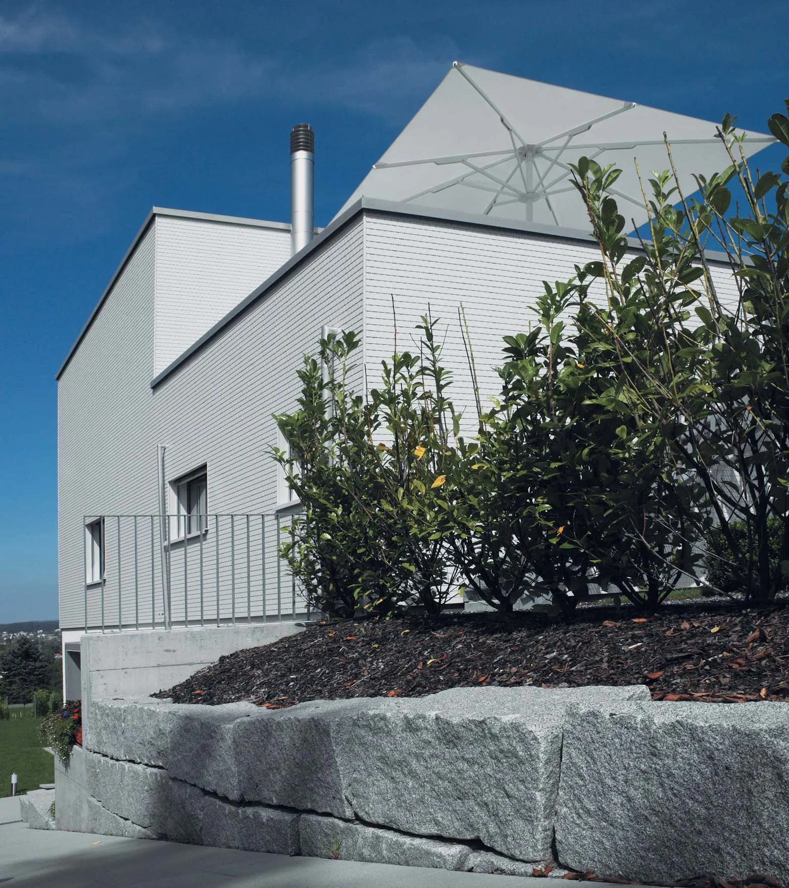 Feingliedrige weisse Faserzementfassade des Hauses in Tägerwilen mit gegliedertem Volumen und Terrasse.