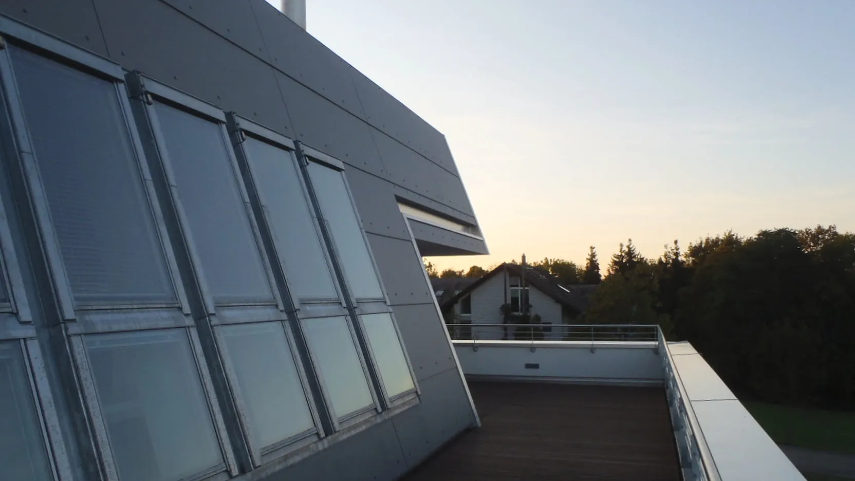 Dunkle geneigte Gebäudehülle mit eingeschnittenen Fenstern und angrenzender geschützter Dachterrasse beim Wohnhaus in Kreuzlingen.