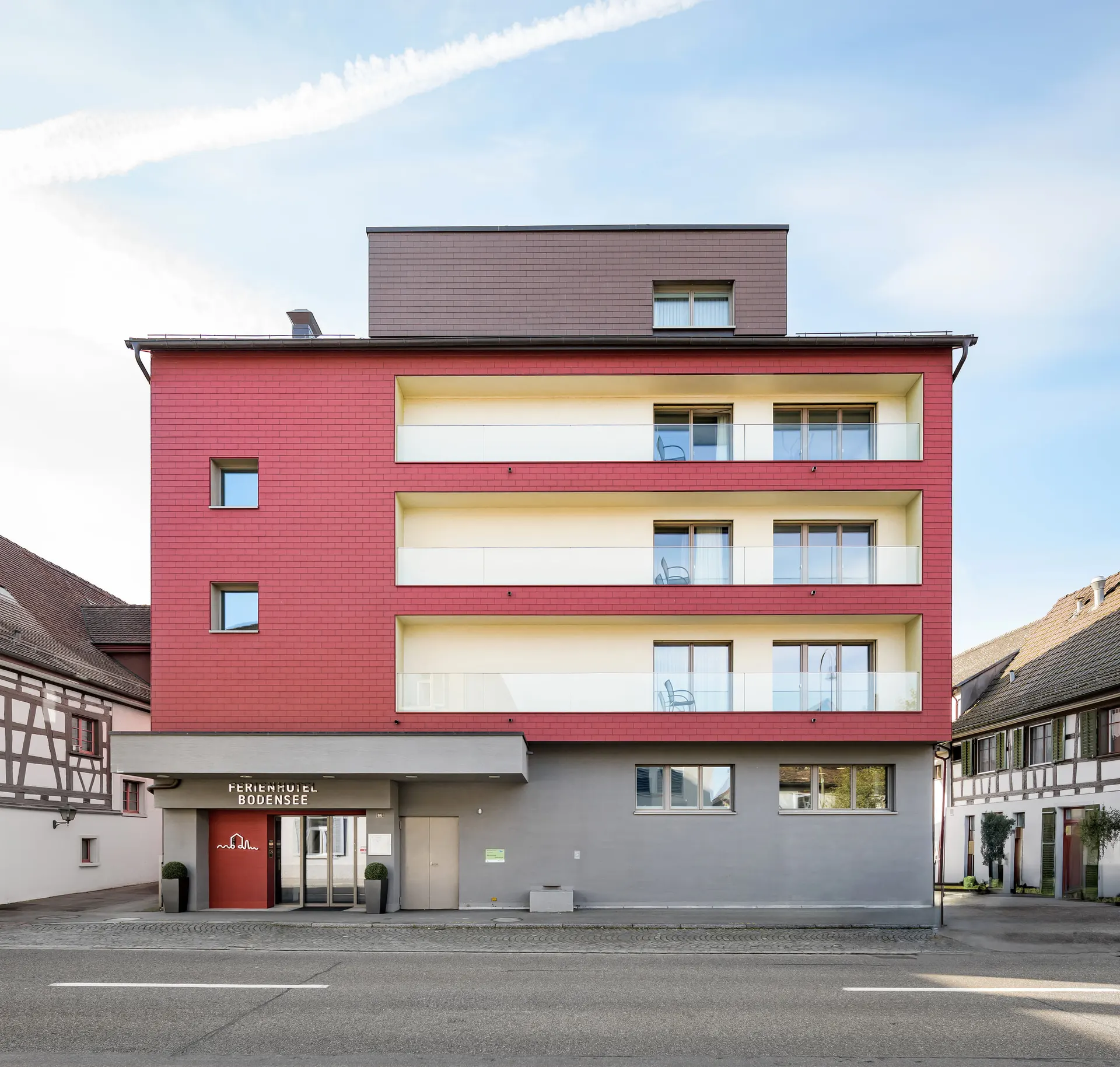 Ferienhotel Bodensee in Berlingen mit roter Fassade und geschützten hellen Loggien zwischen zwei historischen Fachwerkhäusern.